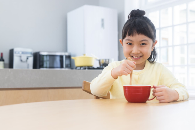 カップのスープをスプーンで混ぜる笑顔の子ども