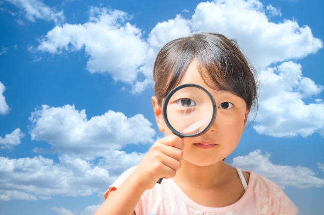 すきっ歯になる原因を虫眼鏡を片手に調べる子ども