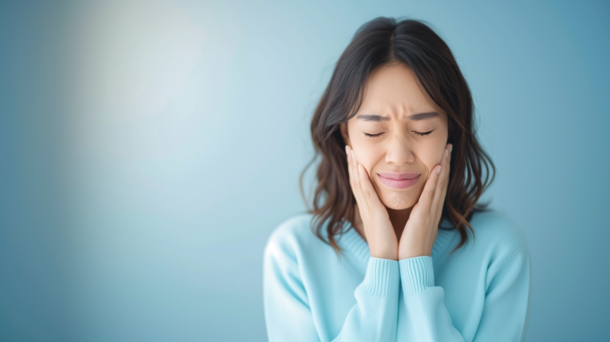 歯が痛んで両手で頬をおさえて耐える矯正中の女性